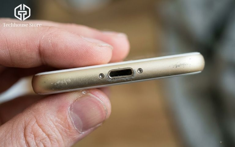 Mua iPhone cũ ở đâu uy tín Hà Nội? Gợi ý 5 địa chỉ & Kinh nghiệm mua an tâm Cận cảnh hai ngón tay đang cầm lật đáy một chiếc iPhone cũ để kiểm tra cổng sạc và hai con ốc vít nhỏ xem có vết xước cạy mở không.