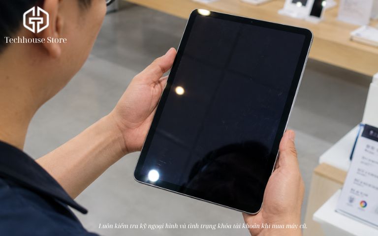 iPad 64GB có đủ dùng không? Tư vấn chọn đúng theo nhu cầu Cận cảnh một người đang cầm nghiêng chiếc iPad dưới ánh sáng đèn để kiểm tra kỹ các góc cạnh và ngoại hình máy tại cửa hàng.