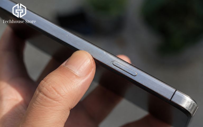 Mua iPhone cũ trả góp tại Hà Nội: cần chuẩn bị những gì? Bức ảnh chụp macro cận cảnh tay người đang cầm chiếc điện thoại, ánh sáng chiếu rõ vào phần viền kim loại để lộ vài vết xước dăm siêu nhỏ, thể hiện tình trạng máy cũ.