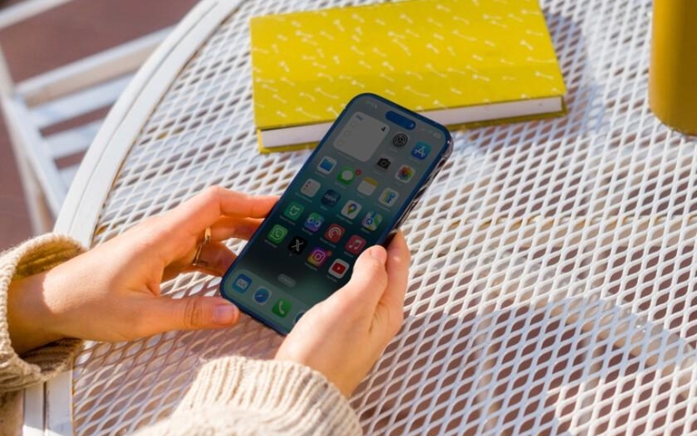 Cách bảo vệ pin iPhone giúp pin bền hơn khi sử dụng Người dùng cầm iPhone ngoài trời dưới ánh nắng mạnh và nhiệt độ cao.