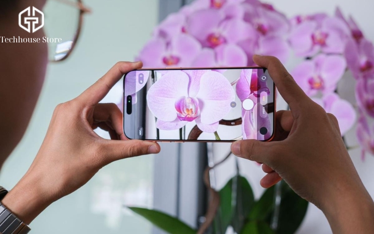 iPhone 18 Pro Max vs iPhone 17 Pro Max: Khác gì, có đáng nâng cấp? Người dùng cầm iPhone Pro Max theo chiều ngang để chụp hoa bằng ứng dụng Camera trong thực tế.