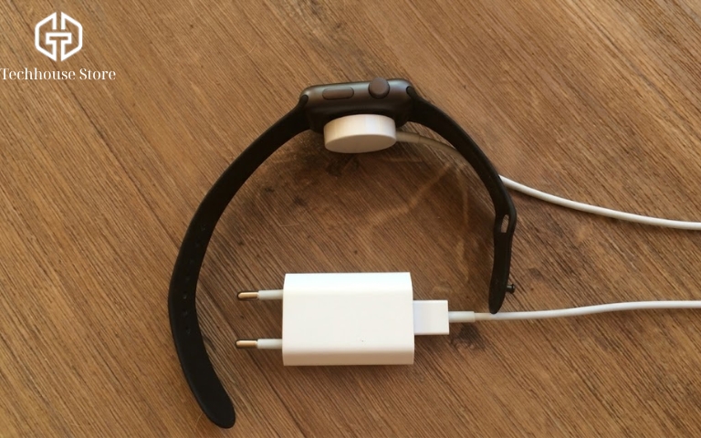 Cách sạc Apple Watch đúng cách cho người mới sử dụng Mặt sau Apple Watch gắn với đầu sạc từ tính màu trắng, bên dưới có dây cáp và củ sạc điện USB-A.